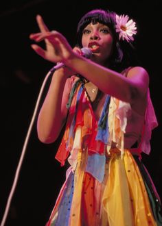 a woman with a flower in her hair is holding a microphone and wearing a colorful dress