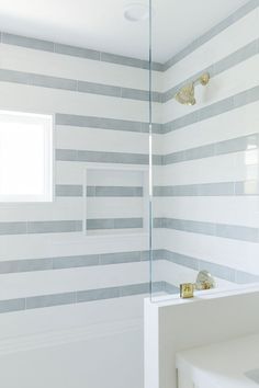 a white and gray bathroom with gold faucet, shower head, and mirror