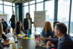 a group of people sitting around a table in front of a whiteboard with writing on it