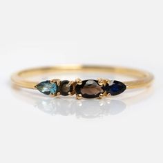 three stone ring in yellow gold with blue and brown stones on the sides, set against a white background