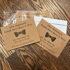 three brown tags with bow ties on them sitting on a wooden table next to envelopes