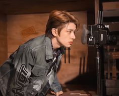 a young man leaning over a desk in front of a camera