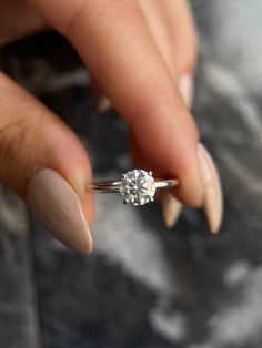 a woman's hand holding a ring with a diamond on it and her nails