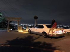 a woman sitting on the back of a white car in front of a city at night