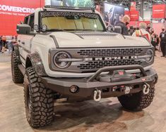 a white truck parked on top of a wooden floor next to other people at a convention