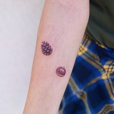 a small pine cone tattoo on the left inner arm, and an acorn in the middle