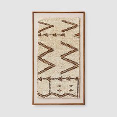 an old rug hanging on the wall in front of a white wall with a wooden frame