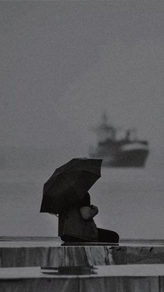 a person sitting on a bench with an umbrella over their head and a boat in the background