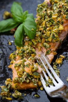 a piece of salmon covered in herbs and seasoning on a plate with a fork