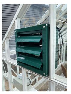 a green ventilator mounted to the side of a glass wall in a greenhouse