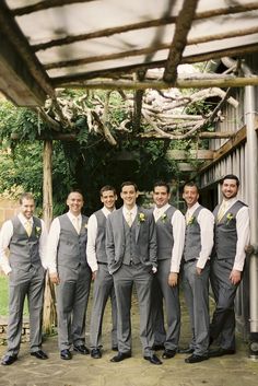 a group of men standing next to each other in front of a wooden structure with trees