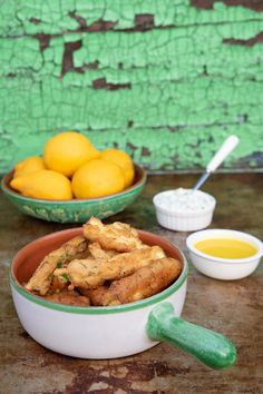 a bowl filled with fried food next to two bowls of lemons and dipping sauce