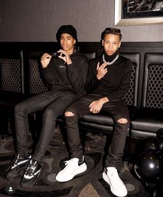 two young men sitting next to each other in front of a black couch and chair