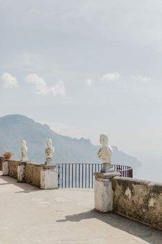 statues on the edge of a building overlooking water and mountains in the distance with clouds overhead