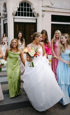 a group of women standing next to each other in front of a building holding bouquets