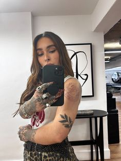 a woman taking a selfie with her cell phone in front of her and tattoos on her arm