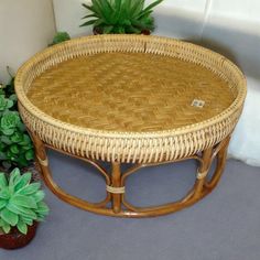 a wicker coffee table sitting on top of a floor next to potted plants