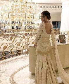 a woman in a white dress standing next to a gold chandelier and marble floor