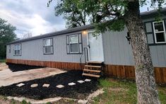 a mobile home sits next to a tree and steps leading up to the front door