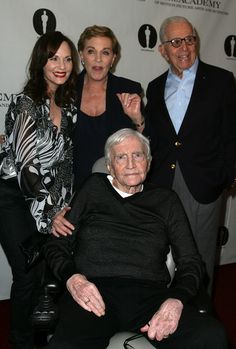 an older man sitting in a wheel chair with two women and one man standing behind him