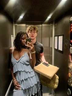 a man and woman standing in an elevator looking at their cell phones while holding a box