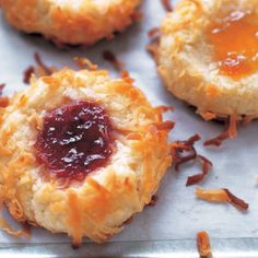 three biscuits with jam on them sitting on a piece of parchment paper next to other pastries