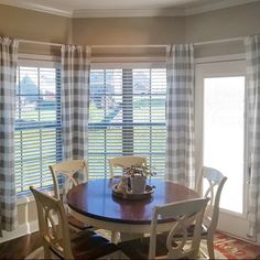 a dining room table with four chairs next to a window covered in plaid drapes