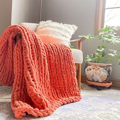 an orange blanket sitting on top of a chair next to a potted plant