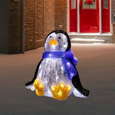 a light up penguin sitting on the ground in front of a building with red doors