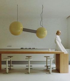 a woman standing in front of a table with stools and lights hanging from it