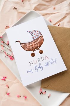 a card with a baby stroller on it sitting on top of a plate next to pink flowers