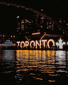 the toronto sign is lit up at night with lights reflecting on the water and buildings in the background