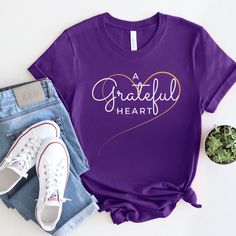 Show the world that a grateful heart is a happy heart with this stylish and meaningful tee. Whether you're layering or wearing it on its own, it is a great way to spread positivity and spread the message of thankfulness. Custom made 100% cotton Light fabric Retail fit Tear away label Runs true to size Cotton T-shirt With Heart Graphic For Fall, Inspirational Cotton T-shirt For Fall, Casual Purple T-shirt As Gift, Cotton Heart Graphic T-shirt For Fall, Relaxed Fit Tops With Heart Graphic For Gifts, Fall Cotton T-shirt With Heart Graphic, Red Team, Spread Positivity, Happy Heart