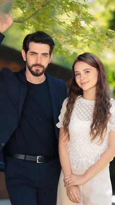 a man and woman standing next to each other in front of a green leafy tree