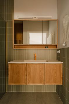 a bathroom with green tiled walls and wooden cabinetry, along with a mirror above the sink