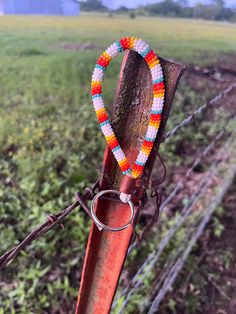 an orange and white beaded bracelet is hanging on a rusted pole in the middle of a field