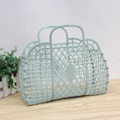 a white basket sitting on top of a wooden table next to a potted plant