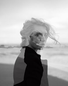 a black and white photo of a woman with her hair blowing in the wind at the beach