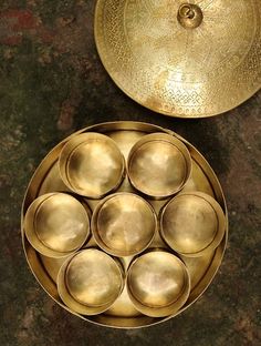 an assortment of metal bowls and plates on a counter top with a gold plate next to it