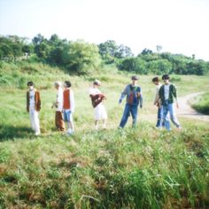 several people are standing in the grass on a hill with their backs to each other