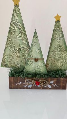 three small christmas trees sitting on top of a wooden box filled with grass and gold stars