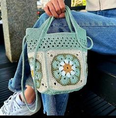 a woman is sitting on a bench holding a crocheted bag with flowers in it