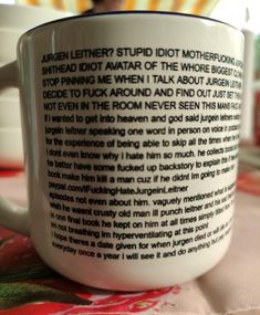 a white coffee mug with black writing on it sitting on top of a tablecloth