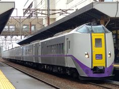 a silver and purple train pulling into a station