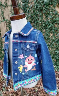 This Baby Shark Denim Jacket is perfect for your little one! Constructed from lightweight denim and detailed with Baby Shark characters, it makes a fun and stylish addition to any wardrobe. With its added ribbon detail, it's sure to be a hit with the little ones. These jackets run TRUE TO SIZE. Please note that jackets are personalized and made to order. They will not always be exact replicas. Denim color may vary. Cute Medium Wash Cotton Outerwear, Cute Cotton Denim Jacket, Blue Cotton Denim Jacket For Playtime, Spring Denim Jacket For Playtime, Playtime Denim Jacket With Pockets, Playful Cotton Denim Jacket With Pockets, Playful Denim Jacket For Fall, Fun Spring Denim Jacket, Long Sleeve Denim Jacket For Playtime