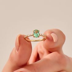 a woman's hand holding an engagement ring with a green stone in the middle