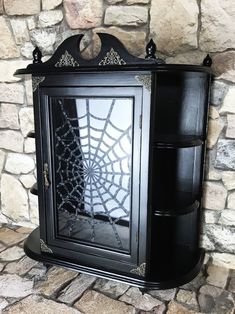 a black cabinet sitting on top of a stone floor next to a wall with a spider web in it