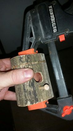 a hand holding a piece of wood with a hole puncher on it's side