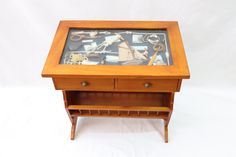 a small wooden table with a glass top and drawer on it's side, holding various items