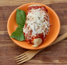 an orange plate topped with lasagna covered in sauce and cheese next to a fork